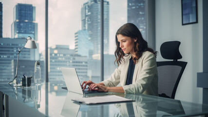 portrait of young successful caucasian businesswoman sitting at desk working on laptop computer in c