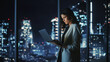 © Gorodenkoff - Big City Modern Office at Night: Successful Young Businesswoman Standing and Using Laptop. Beautiful Female Digital Entrepreneur Thinking of Investment Strategy for e-Commerce Project.