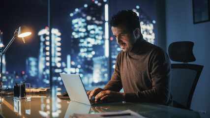 Poster - Portrait of Thoughtful Successful Businessman Working on Laptop Computer in His Big City Office at Night. Charismatic Digital Entrepreneur does Data Analysis for e-Commerce Strategy.