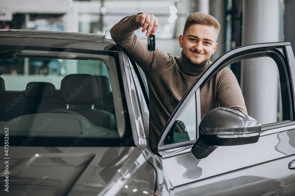 Young handsome man choosing a car in a car showroom