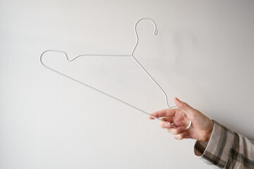 Girl holding an empty white clothes hanger in her hands on a light background. Smart consumption or sales concept