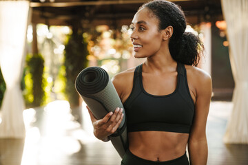 Wall Mural - Black woman smiling at camera while standing with yoga mat