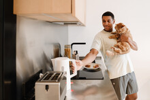 Black Man Wearing T-shirt Holding His Cat While Making Breakfast