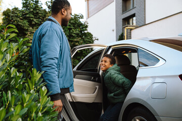 Wall Mural - Black man an his son smiling and talking together while standing by car