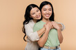 brunette asian woman hugging adult daughter isolated on beige