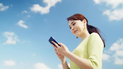 Poster - 青空を背景にスマホを使う女性