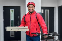 Smiling Deliveryman With Backpack Holding Pizza Boxes And Bicycle In Front Of House