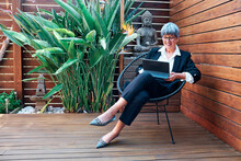 Mature Businesswoman Using Digital Tablet While Sitting On Chair In Backyard