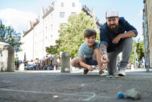 Father Throwing Chalk While Playing With Son On Sidewalk