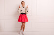 © Look! - Full length slender young caucasian woman crosses her fingers looking up near white wall. Blonde with smile on her face in sweater, skirt and shoes. Hope for luck, concept