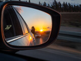 Fototapeta  - The sunset is reflected in the mirror of a car racing down the highway