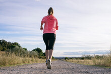 Female Runner Jogging On Country Road During Sunny Day