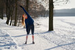 © Westend61 - Young woman stretching while standing on snow during winter