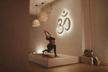 Female Yoga Instructor With Arms Raised Bending While Practicing By Om Symbol