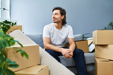 Man Looking Away While Sitting Amidst Cardboard Boxes At Home