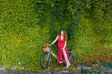 Young Woman Sitting On Bicycle In Front Of Ivy Wall While Looking Away