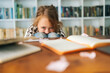 © dikushin - Medium shot portrait of tearing primary child school girl sitting alone hugging knees in front of desk with difficult homework, looking at camera, blurred background, selective focus.