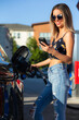 © SuperStock - Young happy woman looking at mobile phone while pumping gas into car.