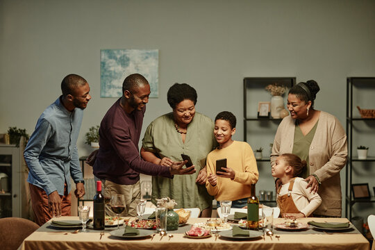 Portrait of big African-American family looking at smartphone screen while enjoying dinner party at home