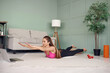 © Admiral - Fit woman doing superman's exercise and watch online workout tutorial on laptop, training in living room