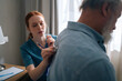 © dikushin - Close-up of female cardiologist doctor examining lungs of elderly senior male patient at home using stethoscope. Nurse listening with stethoscope to back of mature adult man in hospital room.