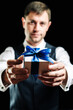 Holding gift box. Happy young business man holding surprise giftbox present with blue ribbon isolated on black background. Present for birthday, valentine day, Christmas, New Year.