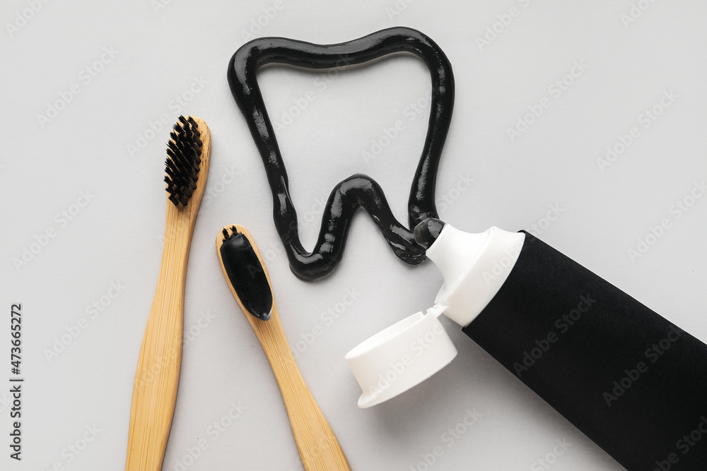Tooth made of black paste, bamboo brushes and tube on light background