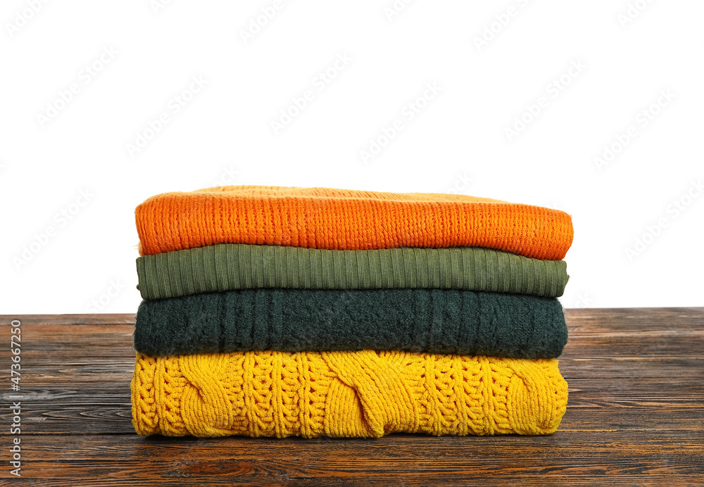 Trendy warm sweaters on wooden table against white background