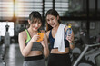 © amnaj - Two smiling Asian woman chatting with a smartphone and holding a water bottle during a gym break.
