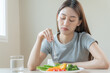 © KMPZZZ - Diet in bored face, unhappy beautiful asian young woman, girl on dieting, holding fork in salad plate, dislike or tired with eat fresh vegetables. Nutrition of clean, healthy food good taste.