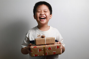 Portrait of a happy Asian boy receiving Christmas gifts, standing against a white wall.