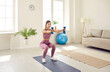 © Studio Romantic - Beautiful young sporty woman squats with dumbbells at home during morning workout. Girl in leggings and top trains on sports mat in living room. Concept of sports and healthy lifestyle.
