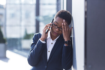 Woman businessman sad complains on the phone, reports bad news, African American woman in despair near the office, holding hands behind his head