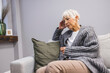 © Dragana Gordic - Beautiful Sad Senior Woman is Looking Downward While Sitting on Couch at Home. A Solemn Elderly Woman Sitting on Her Bed Dealing With Depression. Portrait of worried senior woman sitting on sofa