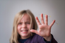 Girl Showing Hand With Pins Pierced In Skin Against Gray Background