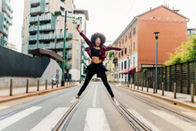 Carefree Woman Jumping With Arms Outstretched On Railroad Tracks