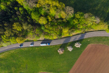 Drone View Of Cars Driving Along Countryside Road Stretching Between Green Grove And Plowed Field