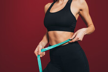 Mid Adult Sportswoman Measuring Waist With Tape Against Maroon Background