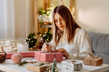 Wall Mural - Woman wrapping Christmas eco natural gift boxes at home. Preparing presents on white table with decor elements, lights and items Christmas or New year DIY packing Concept.