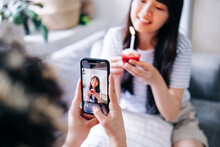 Woman Photographing Female Friend Holding Cupcake Through Smart Phone At Home
