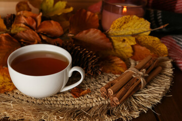 Poster - Cup of hot tea, pine cone, cinnamon sticks and autumn leaves on wooden table. Space for text