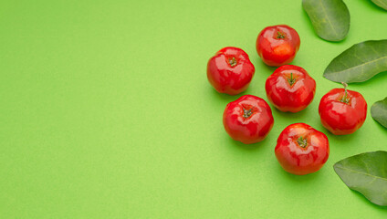 Wall Mural - Ripe red acerola cherries and green leaves isolated on a light green background