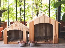 Two Empty Wooden Dog's Houses With Dog Food Bowls  In Balcony Decorated With Houseplant In Plant Pot.