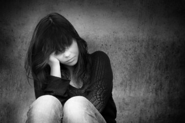 Black and white photo of a sad anonymous young woman who is thoughtful about troubles in front of a gray wall