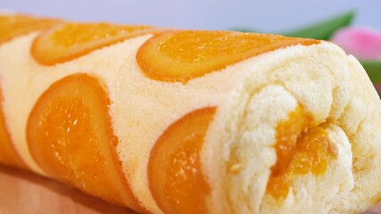 Wall Mural - Motion video close up of orange cake roll with slice orange fruit on wooden plate.