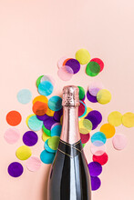 Studio Shot Of Bottle Of Champagne And Colorful Confetti Lying Against Pastel Pink Background