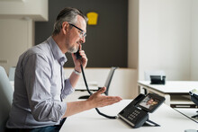 Male Entrepreneur Talking With Colleague Through VoIP Telephone In Office