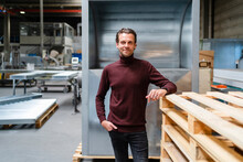 Male Professional With Hand In Pocket Standing By Stack Of Wooden Pallets