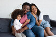 © LIGHTFIELD STUDIOS - mature african american woman smiling at camera while embracing on sofa with young daughter and toddler child