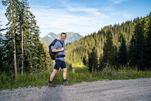 Male Hiker With Backpack Looking Over Shoulder While Walking On Dirt Road